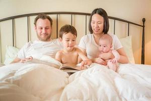 Chinese en Kaukasisch baby jongens lezing een boek in bed met hun ouders foto