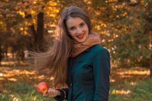 schattig meisje met lang haar- staat in de park en houdt appel in hand- foto