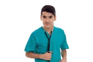 jong knap brunette Mens dokter in blauw uniform met stethoscoop Aan zijn schouders op zoek Bij de camera geïsoleerd Aan wit achtergrond foto