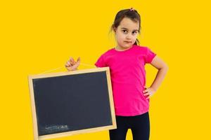 schattig weinig meisje Holding een schoolbord, geïsoleerd geel achtergrond foto