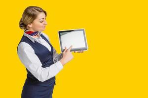 jong vrouw professioneel stewardess staand geïsoleerd Aan muur Holding digitaal tablet tonen scherm op zoek camera glimlachen vriendelijk geel, oranje, achtergrond foto