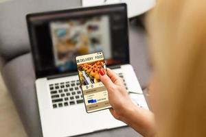 vrouw gebruik makend van laptop en smartphone in cafe Holding telefoon met app levering voedsel scherm foto