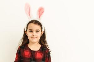 verrast weinig meisje vervelend konijn oren, aan het liegen Aan licht Aan Pasen vakantie. foto