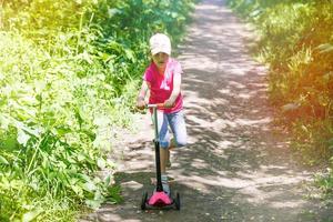 kind rijden scooter. kind Aan kleurrijk trap bord. actief buitenshuis pret voor kinderen. zomer sport- voor peuter- kinderen. weinig meisje in voorjaar park foto