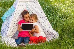 twee gelukkig weinig kinderen zijn zittend Aan de gras en lezing fee verhalen in de buurt een tent in hun huis tuin. huis camping vakantie concept foto