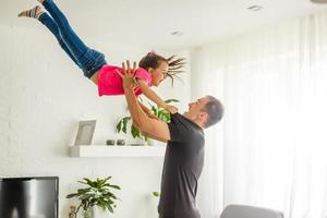 ik kan vlieg. gelukkig vader is hijs- omhoog zijn weinig dochter terwijl staand in leven kamer. foto