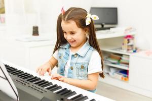 mooi weinig kind meisje spelen piano in leven kamer of muziek- school. peuter- kind hebben pret met aan het leren naar Speel muziek- instrument. opleiding, vaardigheden concept foto