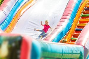 weinig meisje zittend Aan opblaasbaar trampolinespringen. de kind is rijden hoog in een schuiven. foto