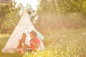 twee gelukkig lachend weinig meisjes in camping tent in paardebloem veld- foto