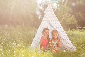 twee gelukkig lachend weinig meisjes in camping tent in paardebloem veld- foto