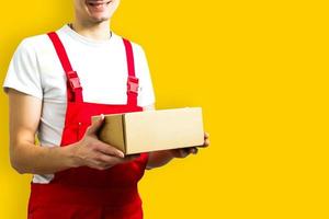 magiër van een gelukkig jong levering Mens in rood pet staand met pakket post doos geïsoleerd over- geel achtergrond foto