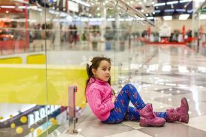 een weinig meisje Aan de achtergrond van een boodschappen doen centrum. foto