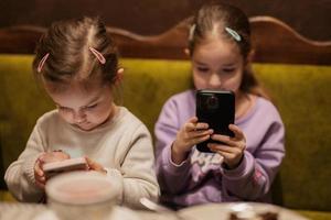 zussen kinderen houden mobiel telefoon samen Bij knus cafe en hebben plezier. foto