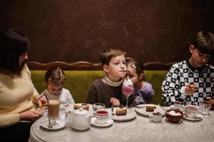 gelukkig familie aan het eten desserts samen Bij knus cafe en hebben plezier. jongen kind drinken melk schudden. foto