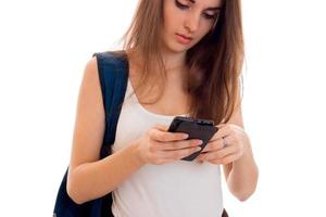 mooi jong studenten meisje met blauw rugzak Aan schouder en mobiel telefoon in handen poseren geïsoleerd Aan wit achtergrond foto