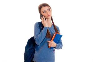 mooi jong brunette leerling meisje met blauw rugzak pratend telefoon geïsoleerd Aan wit achtergrond foto