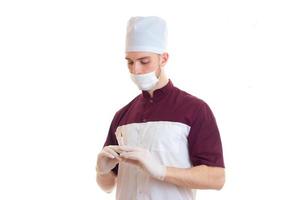 een jong dokter in een hoed en met een masker Aan zijn gezicht Holding een injectiespuit is geïsoleerd Aan een wit achtergrond foto