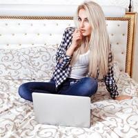 charmant jong blond vrouw met laptop computer zit Aan bed foto