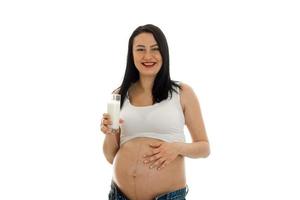 jong vrolijk zwanger moeder geïsoleerd Aan wit achtergrond in studio lachend en poseren met glas van melk foto