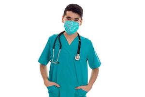 mooi elegant dokter in blauw uniform met stethoscoop en masker poseren en op zoek Bij de camera geïsoleerd Aan wit achtergrond foto