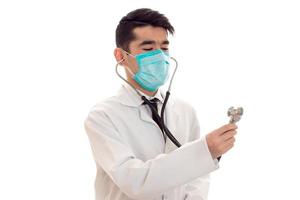 portret van mooi jong brunette mannetje dokter in uniform en masker met stethoscoop poseren geïsoleerd Aan wit achtergrond foto