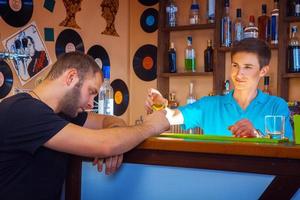 barman geeft kort cocktail naar dronken ongeschoren Mens Bij bar tafel foto