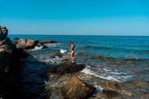 slank jong dame staat Aan de rotsen Bij de zee foto