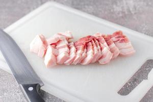 buikspek varkensvlees is gesneden Aan een wit hakken bord in de keuken.sluiten omhoog snijdend glijbaan varkensvlees buik rauw foto