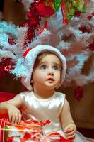 weinig baby opent Cadeau onder de Kerstmis boom foto