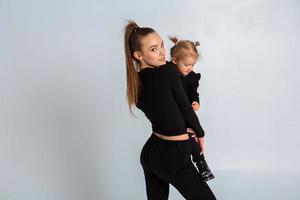 sexy jong moeder in zwart kleren houden haar weinig dochter in handen foto