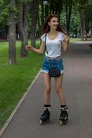 gelukkig jong meisje lachend en skates Aan rol Bij de park foto