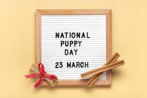 voelde bord met tekst nationaal puppy dag in 23 maart, hond accessoires - bot met rood boog Aan beige achtergrond top visie vlak leggen vakantie kaart foto