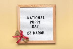 voelde bord met tekst nationaal puppy dag in 23 maart, hond accessoires - bot met rood boog Aan beige achtergrond top visie vlak leggen vakantie kaart foto