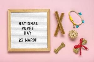 voelde bord met tekst nationaal puppy dag in 23 maart, hond accessoires - lepel, bal, bot, halsband Aan roze achtergrond top visie vlak leggen vakantie kaart foto