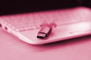 USB flash geheugen kaart met boog leugens Aan een deken van zacht en harig fleece kleding stof beeld afgezwakt in viva magenta, kleur van de 2023 jaar foto