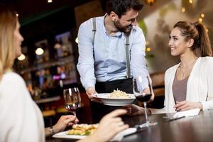 jong ober portie voedsel naar vrouw klanten in de restaurant foto