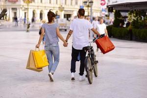 portret van vrolijk Kaukasisch jong paar Mens en vrouw Holding veel papier Tassen na boodschappen doen terwijl wandelen en pratend Aan straat. gelukkig familie paar met pakketjes buitenshuis. buying concept foto