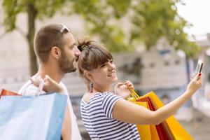 portret van vrolijk Kaukasisch jong paar Mens en vrouw Holding veel papier Tassen na boodschappen doen terwijl wandelen en pratend Aan straat. gelukkig familie paar met pakketjes buitenshuis. buying concept foto