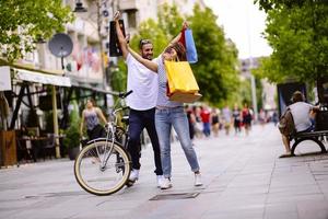 portret van vrolijk Kaukasisch jong paar Mens en vrouw Holding veel papier Tassen na boodschappen doen terwijl wandelen en pratend Aan straat. gelukkig familie paar met pakketjes buitenshuis. buying concept foto