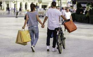 portret van vrolijk Kaukasisch jong paar Mens en vrouw Holding veel papier Tassen na boodschappen doen terwijl wandelen en pratend Aan straat. gelukkig familie paar met pakketjes buitenshuis. buying concept foto