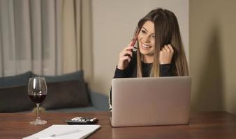mooi jong vrouw in gewoontjes kleding gebruik makend van laptop en glimlachen terwijl werken binnenshuis foto