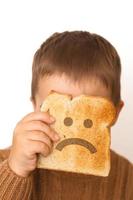 kinderen en gluten. peuter- jongen met geroosterd brood, met verdrietig emoji. gluten onverdraagzaamheid door kinderen. foto