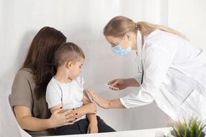 covid 19 vaccin voor kinderen. weinig Kaukasisch jongen krijgen gevaccineerd van covid19. een jong vrouw dokter Holding injectiespuit met coronavirus vaccin. risico en infectie controle concept. foto