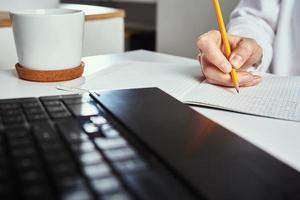 afgelegen werk. vrouw maakt aantekeningen in notitieboekje en gebruik makend van laptop voor studie. foto