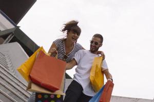 portret van vrolijk Kaukasisch jong paar Mens en vrouw Holding veel papier Tassen na boodschappen doen terwijl wandelen en pratend Aan straat. gelukkig familie paar met pakketjes buitenshuis. buying concept foto