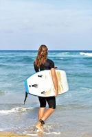 een Mens is staand met een surfen in zijn handen Aan de zee oever. foto