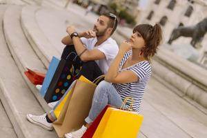 portret van vrolijk Kaukasisch jong paar Mens en vrouw Holding veel papier Tassen na boodschappen doen terwijl wandelen en pratend Aan straat. gelukkig familie paar met pakketjes buitenshuis. buying concept foto