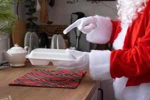 voedsel levering naar huis onderhoud containers in handen van de kerstman claus zet het Aan keuken tafel en duurt het weg. kant en klaar heet bestellen, kerstmis, nieuw jaar vakantie horeca. foto