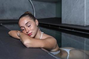 jong vrouw sluitend ogen en ontspannende in zwembad foto