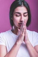 jong vrouw Holding handen in bidden in de buurt mond, voelt zelfverzekerd foto